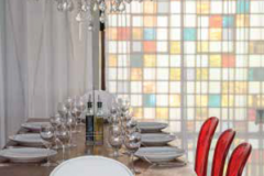 The acrylic Philippe Starck Ghost chairs, a gauzy curtain, a 1950s wall of colored glass, and a vintage chandelier provide contemporary glamour at the waterfront Río Mar.